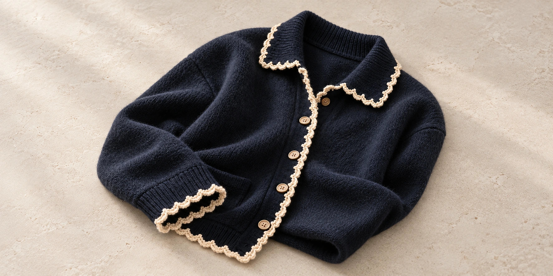A navy cashmere cardigan with ivory crochet along its collar, opening and cuff — collection concept